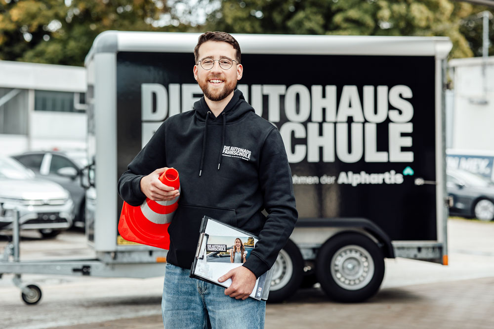 Motorradschüler in Schutzkleidung sitzt auf einem Motorrad, neben ihm steht der Fahrlehrer mit Headset auf einem Übungsplatz.